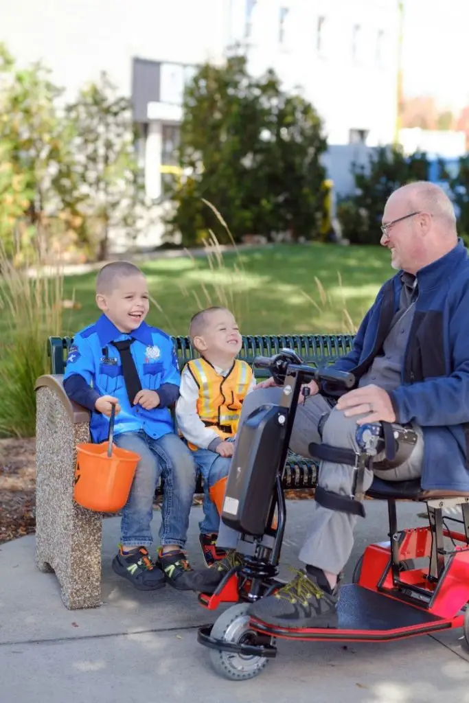 A man in a powered wheelchair laughing with two children