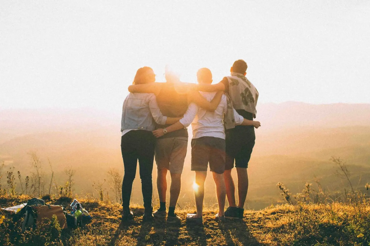 Four adults with arms around each other, in front of a sunset
